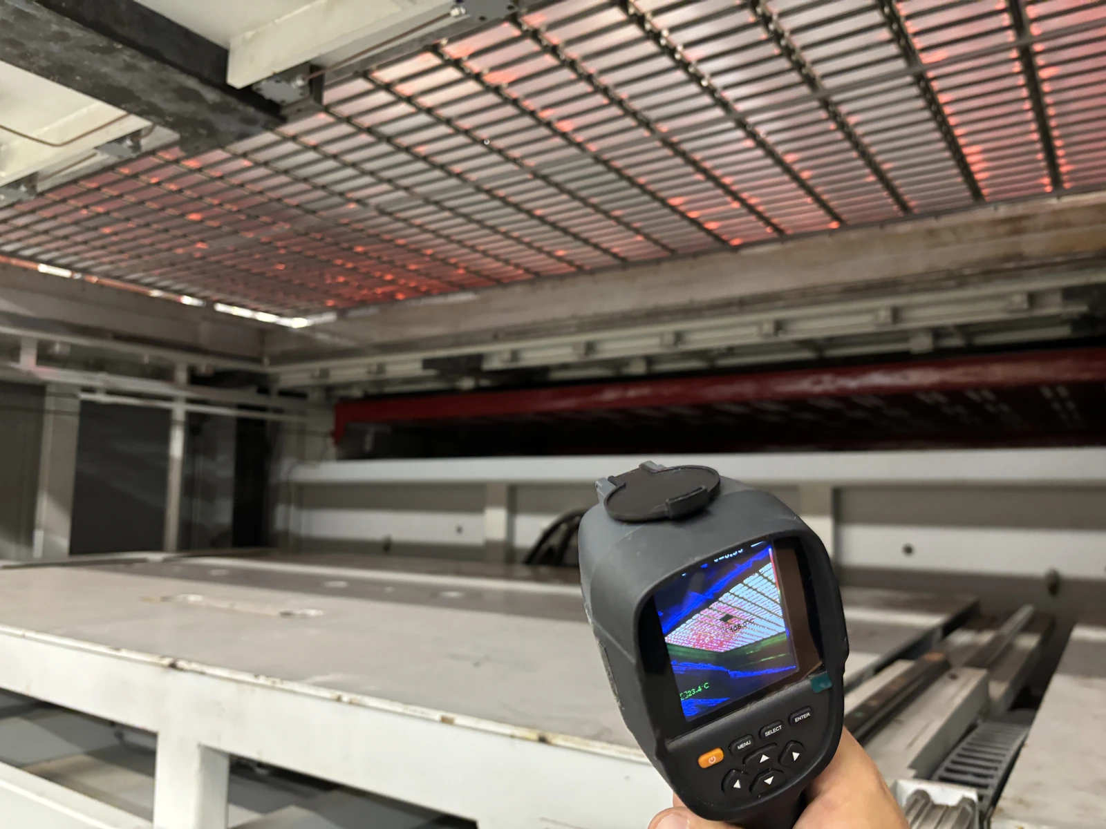 A hand holding a thermal camera in front of an illuminated machine heater array.