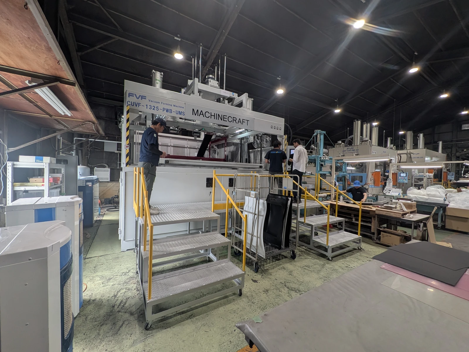 People working around a Machinecraft machine with access stairs and yellow rails during installation in Japan.